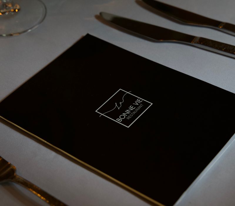 Zwart menu met het elegante logo van La Bonne Vie, gepresenteerd op een strak gedekte tafel.